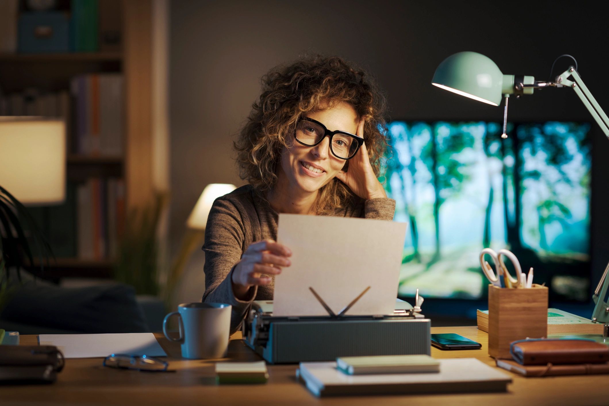 Woman working late on a laptop with a thoughtful smile.